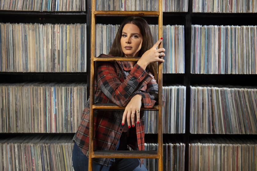 Lana Del Rey peeks through a ladder in front of shelves of vinyl records