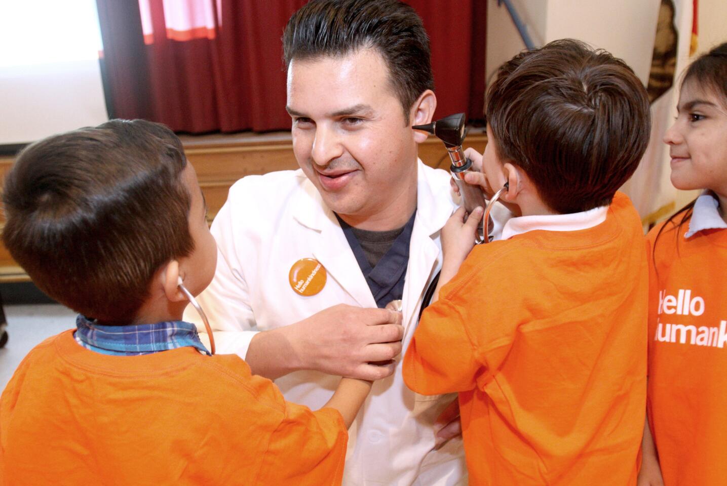 After speaking about being a good neighbor and eating healthy foods, Dignity Health Glendale Memorial Hospital Family Medicine Doctor Antonio Zamorano gets checked out by eager transitional Kindergarten students at Cerritos Elementary School in Glendale on Thursday, Jan. 28, 2016. Dr. Zamorano, who came out with a Batman mask, also showed children some of the items used by doctors at the hospital, including a syringe, needle and stitches and stethoscope.