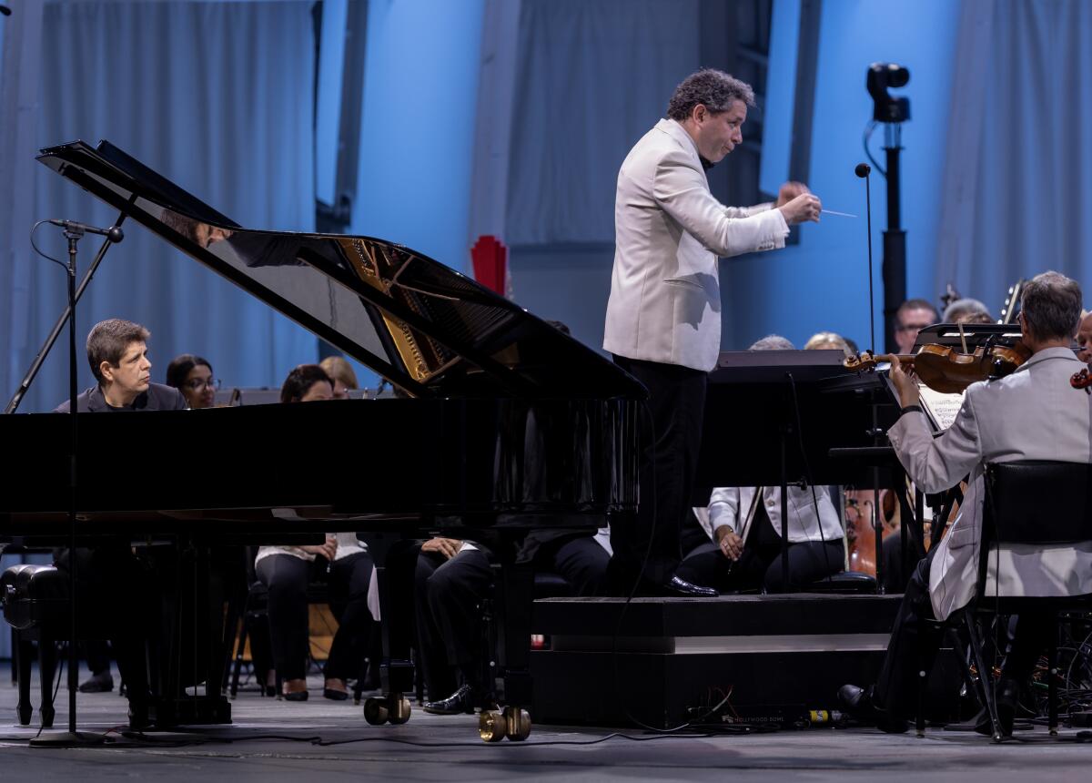 A man dressed in black sits at a grand piano as a conductor in a white jacket leads the L.A. Phil.