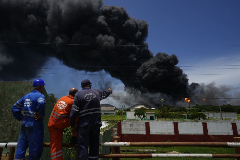 Workers of the Cuba Oil Union, known by the Spanish acronym CUPET, watch a huge rising plume of smoke from the Matanzas Supertanker Base, as firefighters work to quell a blaze which began during a thunderstorm the night before, in Matazanas, Cuba, Saturday, Aug. 6, 2022. Cuban authorities say lightning struck a crude oil storage tank at the base, causing a fire that led to four explosions which injured more than 50 people. (AP Photo/Ramon Espinosa)