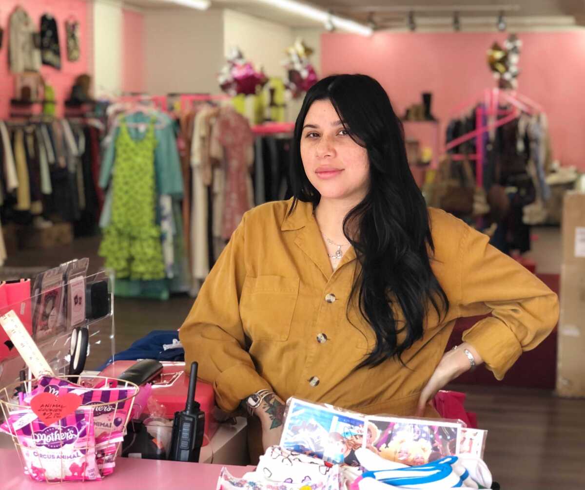 A woman standing behind the counter of a boutique with pink walls