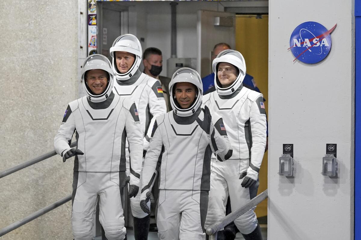 Four astronauts in white space suits walk out of a door