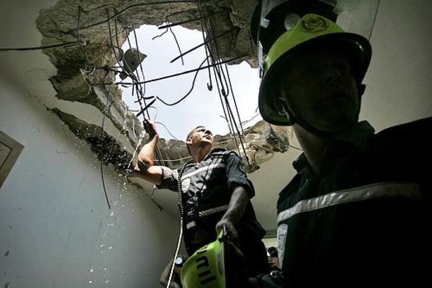 Emergency response workers examine a hole in the roof left when a Hezbollah rocket slammed into an apartment building in Kiryat Shmona. The rocket went through the roof and the third floor, leaving three people lightly injured.