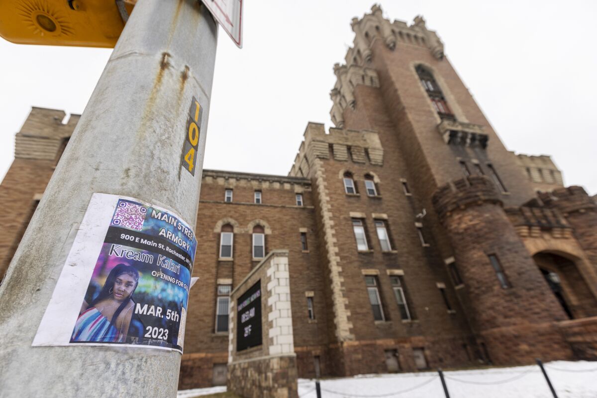 A flyer for a concert hangs on a light post outside a tall brick building