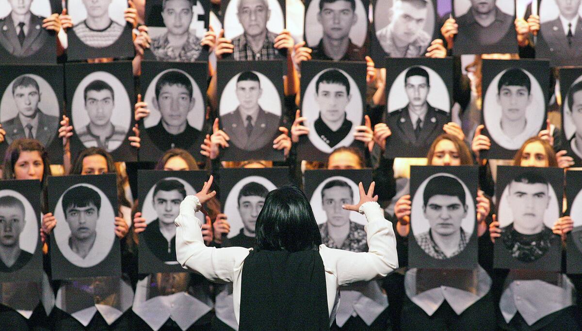 The director of the Rose and Alex Pilibos Student Choir directs a section of the choir who are holding portraits in front of them at the city of Glendale's 15th annual Armenian Genocide commemoration at the Alex Theatre in Glendale on Friday, April 22, 2016.