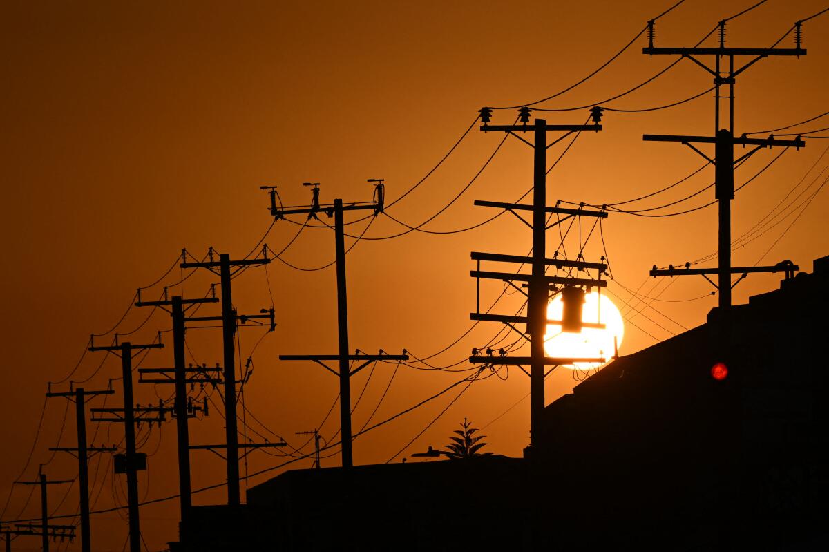 The sun sets behind power lines near homes during a heat wave