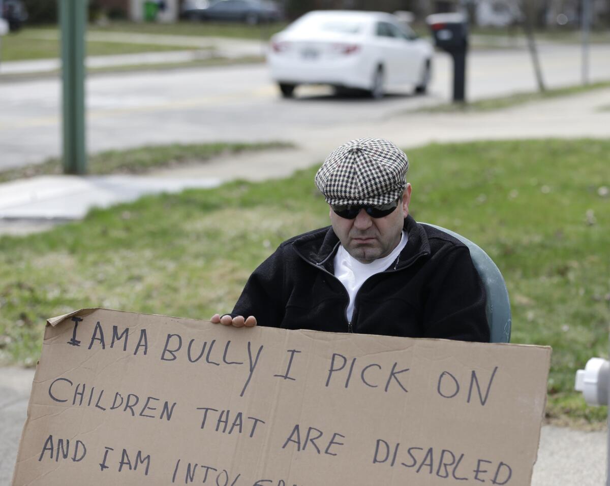 Edmond Aviv sits on a street corner holding a in South Euclid, Ohio declaring he's a bully, a requirement of his sentence because he was accused of harassing a neighbor and her disabled children for the past 15 years.