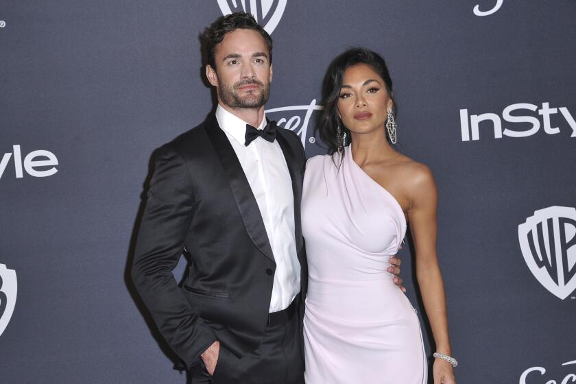 A man with dark hair and facial hair in a tuxedo standing to the left of Nicole Scherzinger in a pink one-shoulder gown