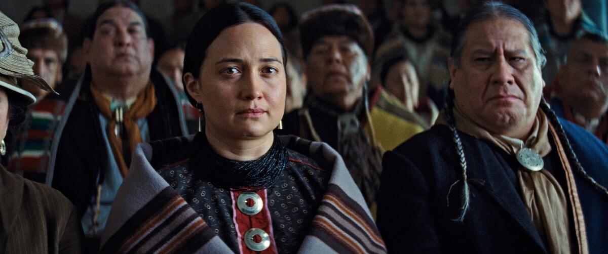 An Indigenous woman and older man stand in a crowd in "Killers of the Flower Moon."
