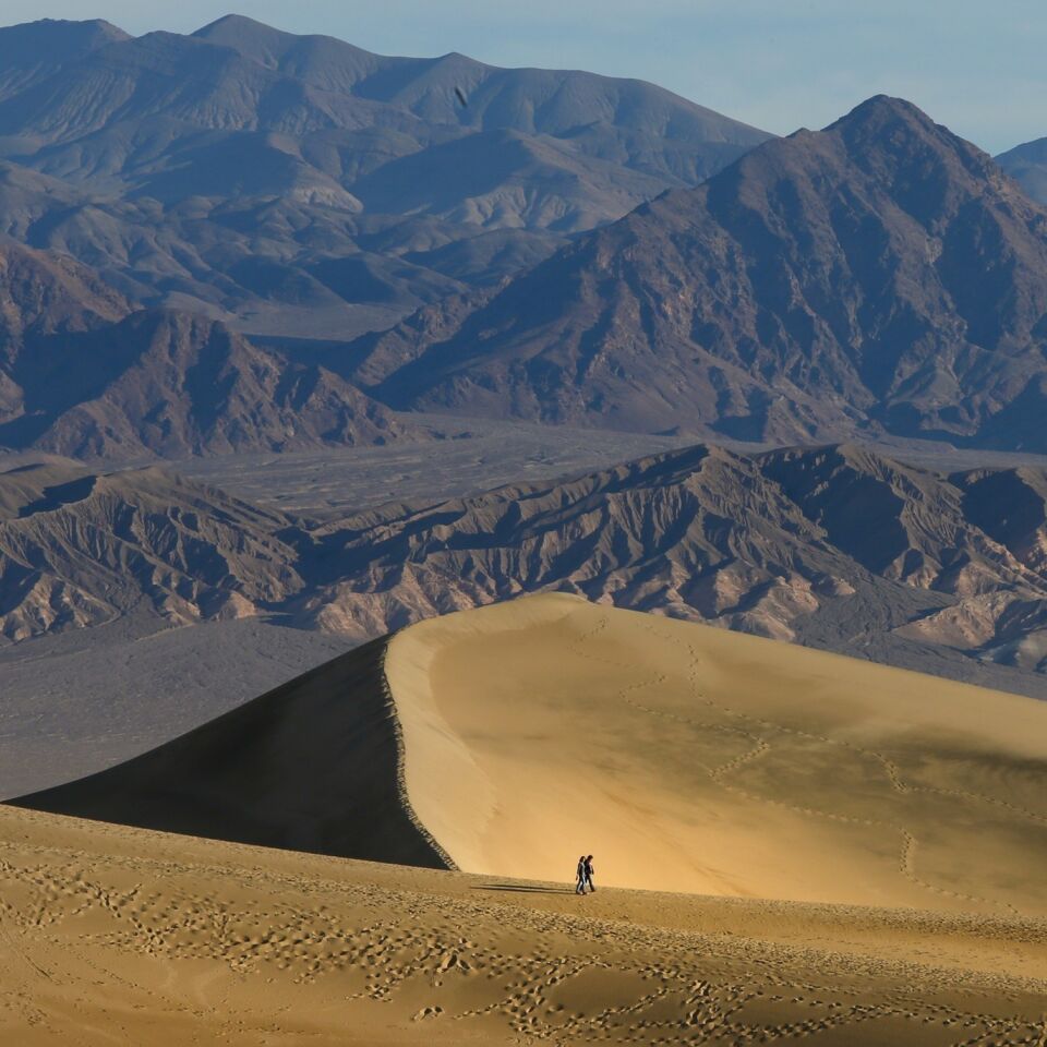 A couple out for an early morning walk in the Mesquite Flat Sand Dunes are dwarfed by the surrounding landscape.