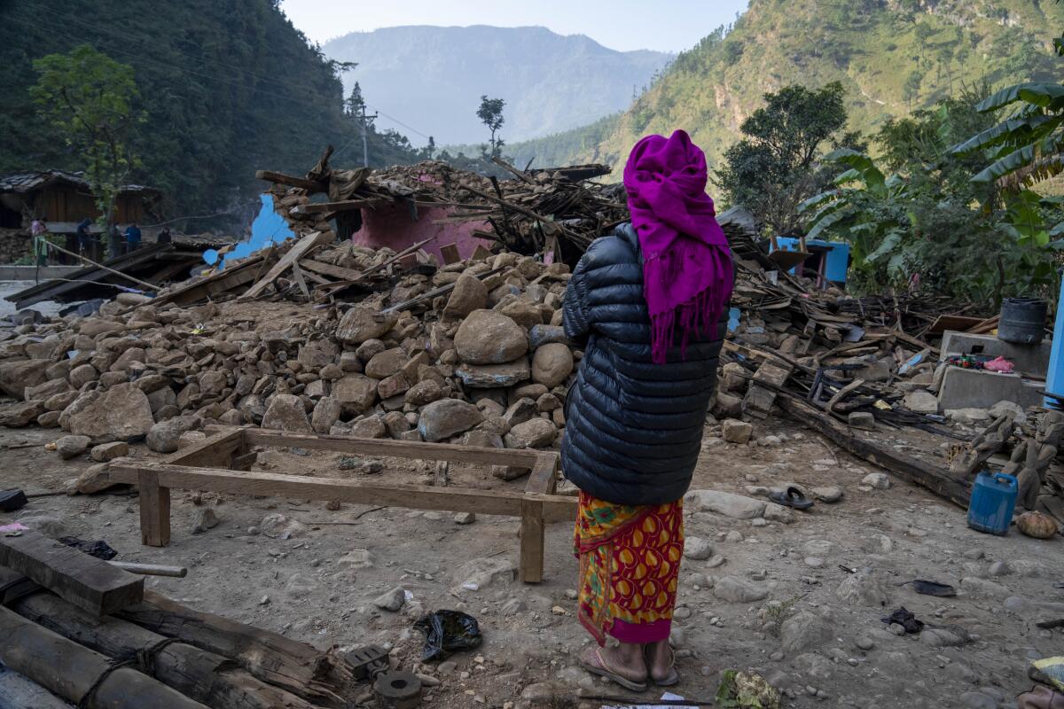 A woman looks at the rubble of her home.