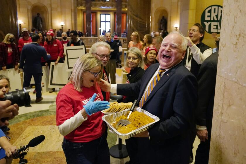 Minnesota Gov. Tim Walz, right, hands out pumpkin bars to a gun safety advocate before the first day of the 2023 Legislative session, Tuesday, Jan. 3, 2023, in St. Paul, Minn. (AP Photo/Abbie Parr)