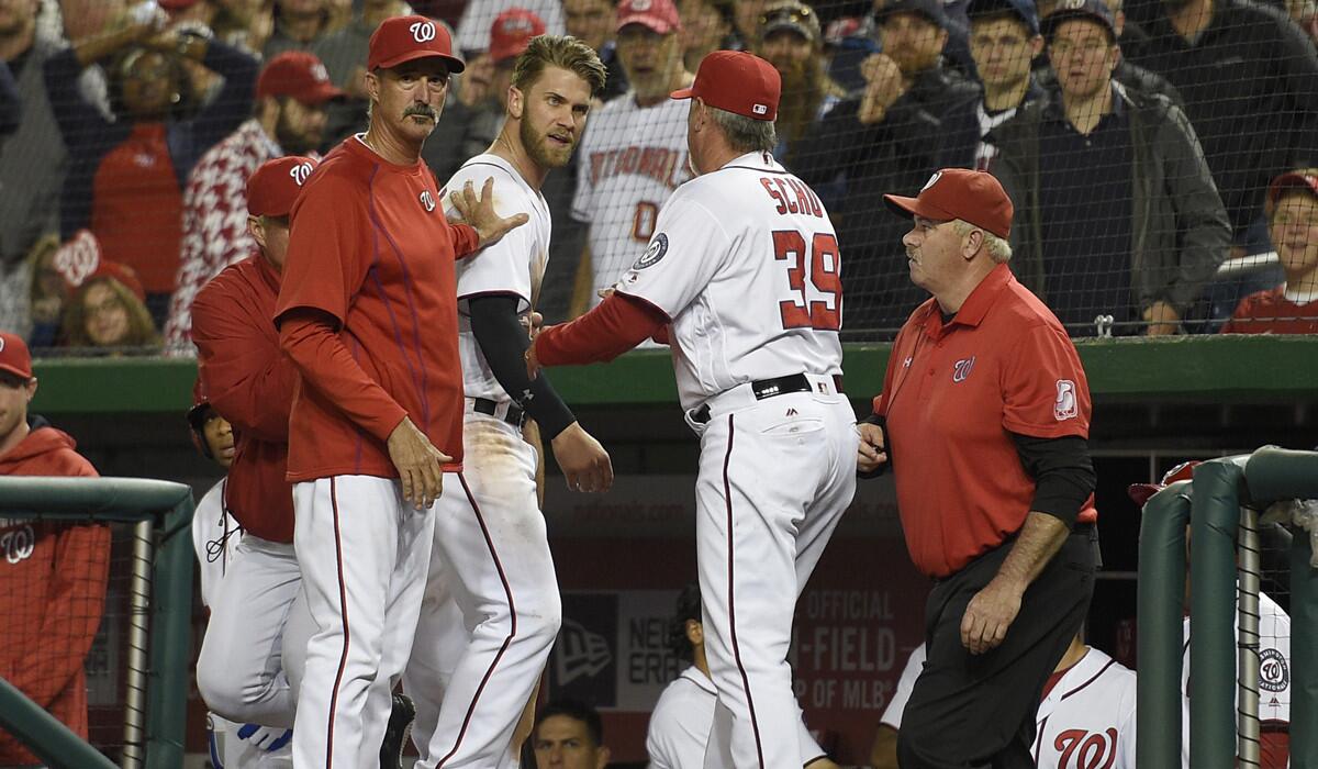 Washington Nationals' Bryce Harper, center, is restrained by pitching coach Mike Maddux, left, and hitting coach Rick Schu (39) after Harper was ejected in the dugout during the ninth inning of an interleague baseball game against the Detroit Tigers on Monday.