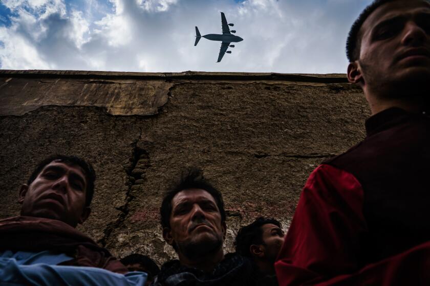 A military transport plane flies over relatives and neighbors of the Ahmadi family as they gather around an incinerated husk of a vehicle destroyed by a U.S. drone strike in Kabul, Afghanistan. In August, life came to a standstill as the Taliban offensive reached the gates of the Afghan capital, sending it into a panic. President Ashraf Ghani escaped; American-backed Afghan forces pulled back. The Taliban swiftly took over a nation that had changed much since it first ruled two decades ago. Jarring, violent scenes followed, marking a tragic coda to a messy and controversial 20-year occupation. The U.S. was ending its longest war.