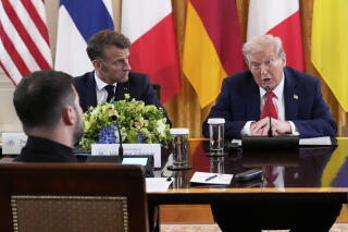 A man seated across from two men, one in red tie and speaking, and the other listening