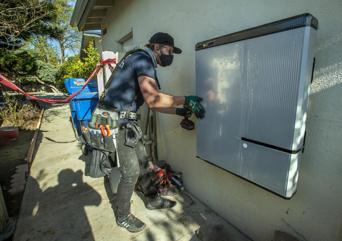 An employee of rooftop solar company Sunrun helps install a lithium-ion battery at a home in Granada Hills in 2020.