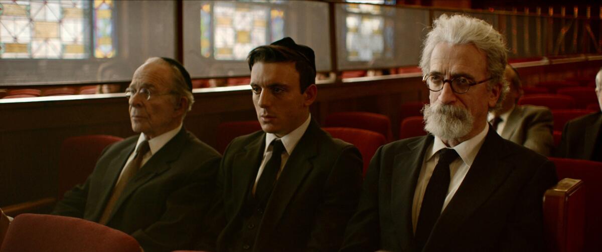 Three men in suits sit in a temple in the movie “Minyan.”
