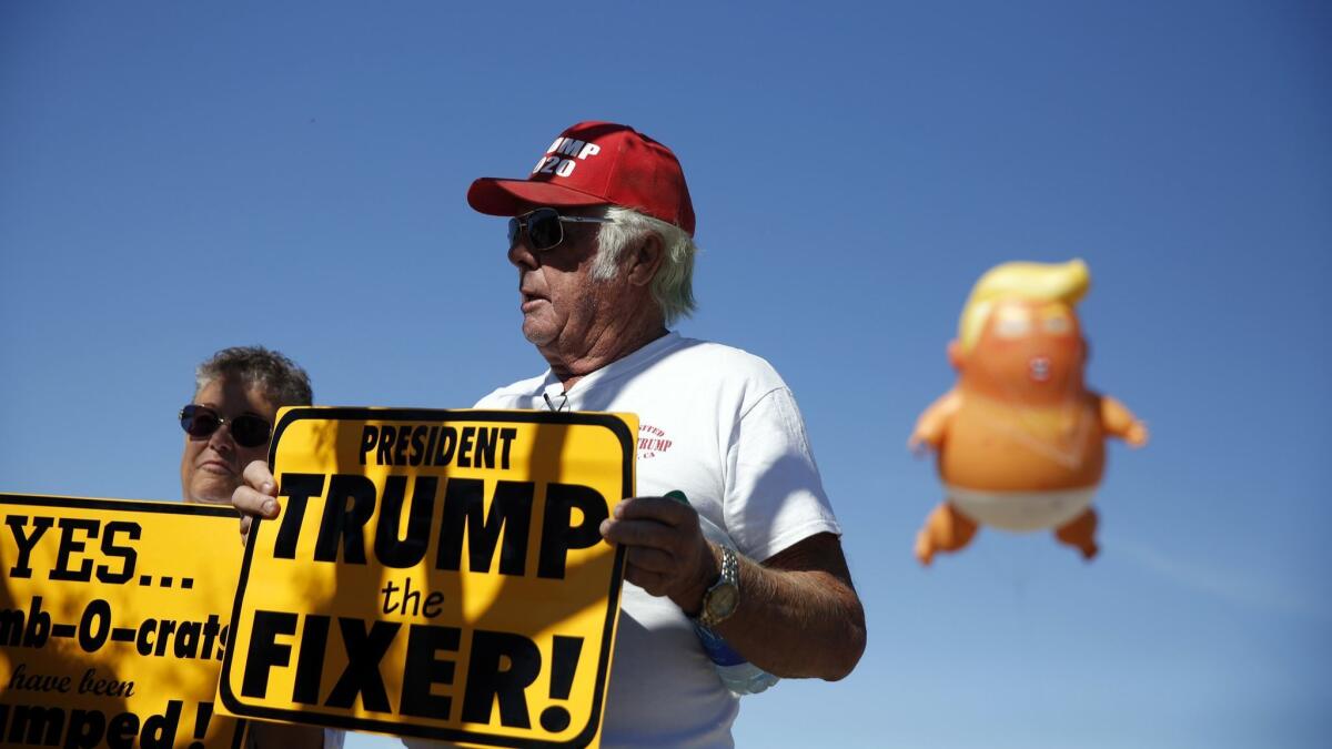 A giant inflatable baby Trump floats above Trump supporters Linda Jung, left, and Keith Wood as they watch protesters make their way to Gran Plaza Outlets.