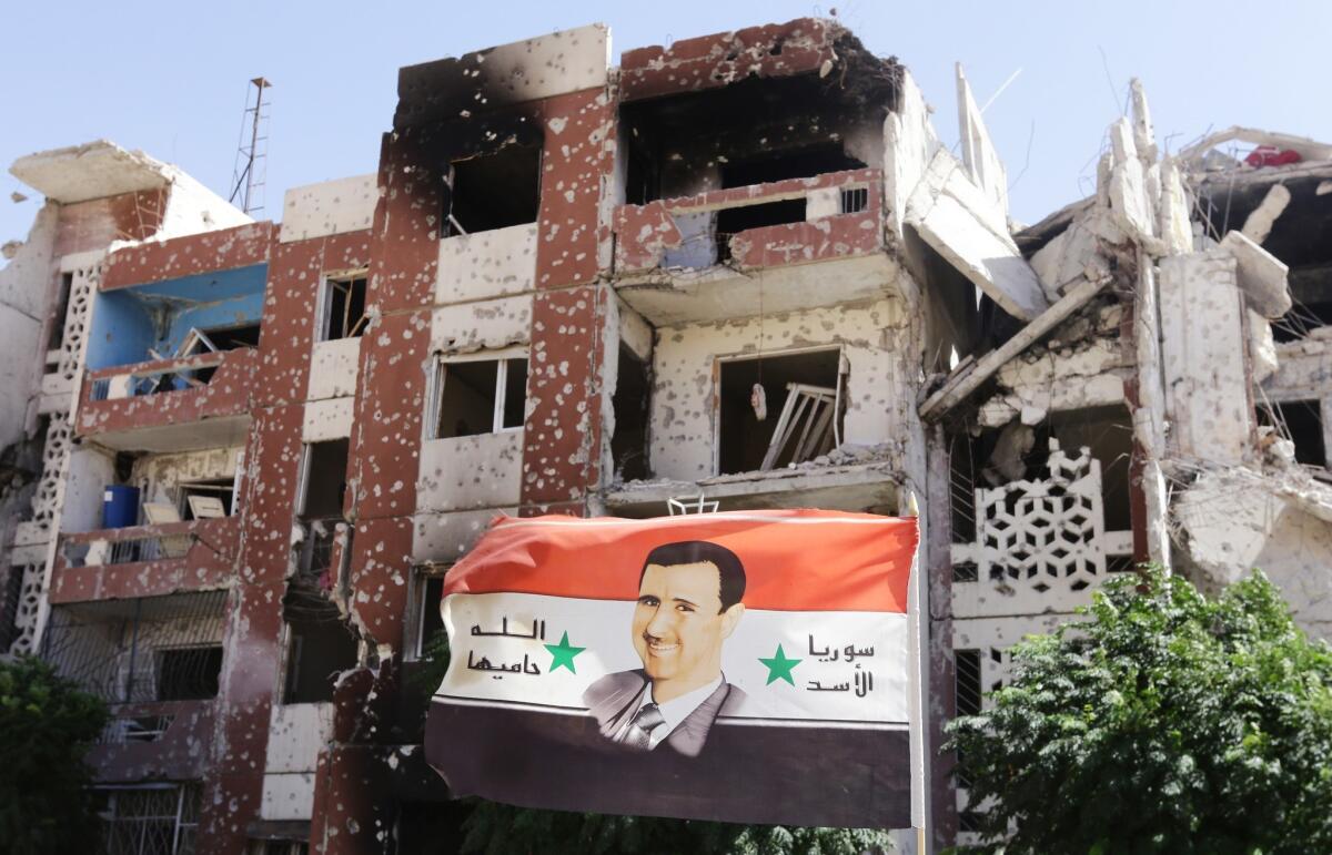 A flag showing Syrian President Bashar al-Assad flutters near damaged buildings in Adra northeast of the capital Damascus in September.