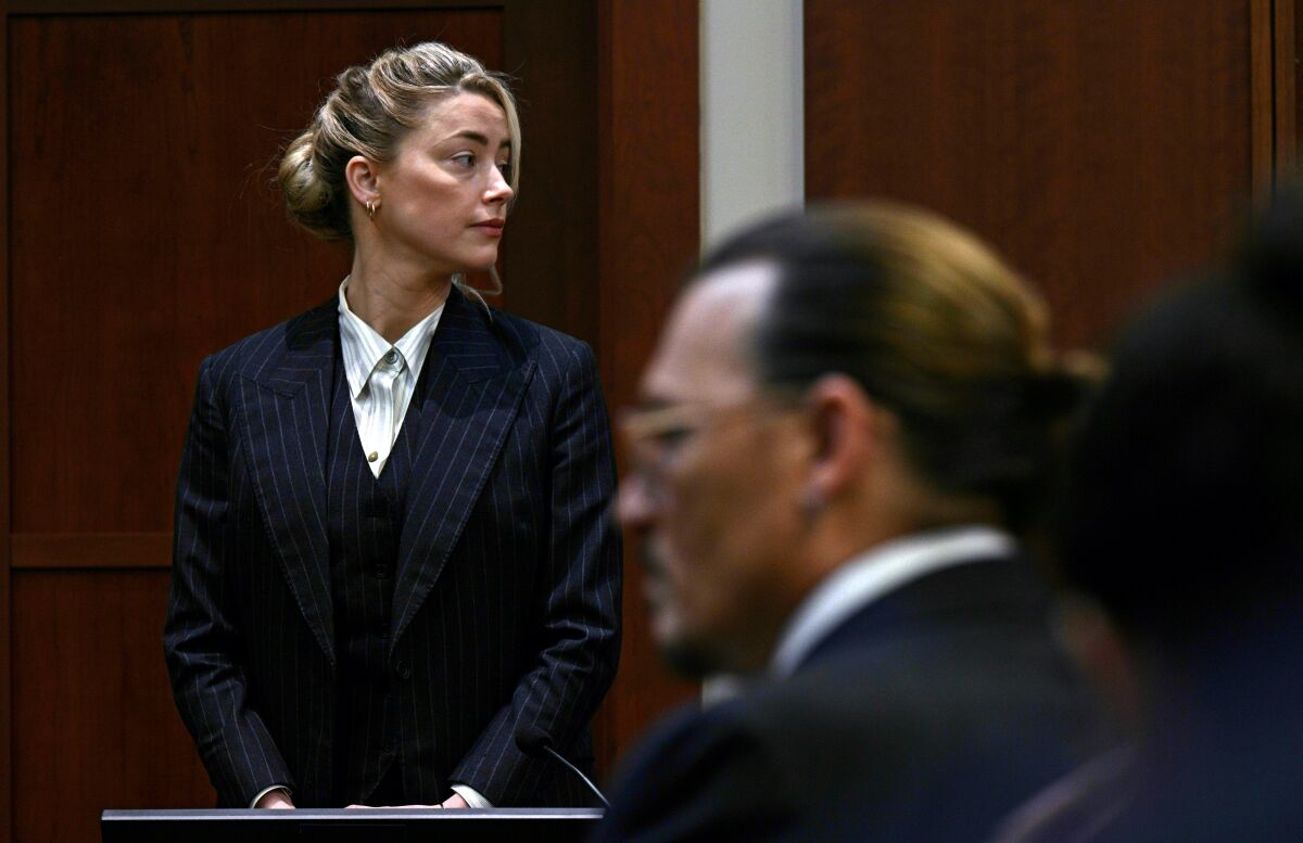 A woman in a courtroom with a man's profile in the foreground