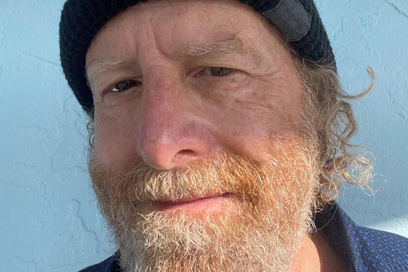 A man with a beard wearing black knit cap and smiling slightly.