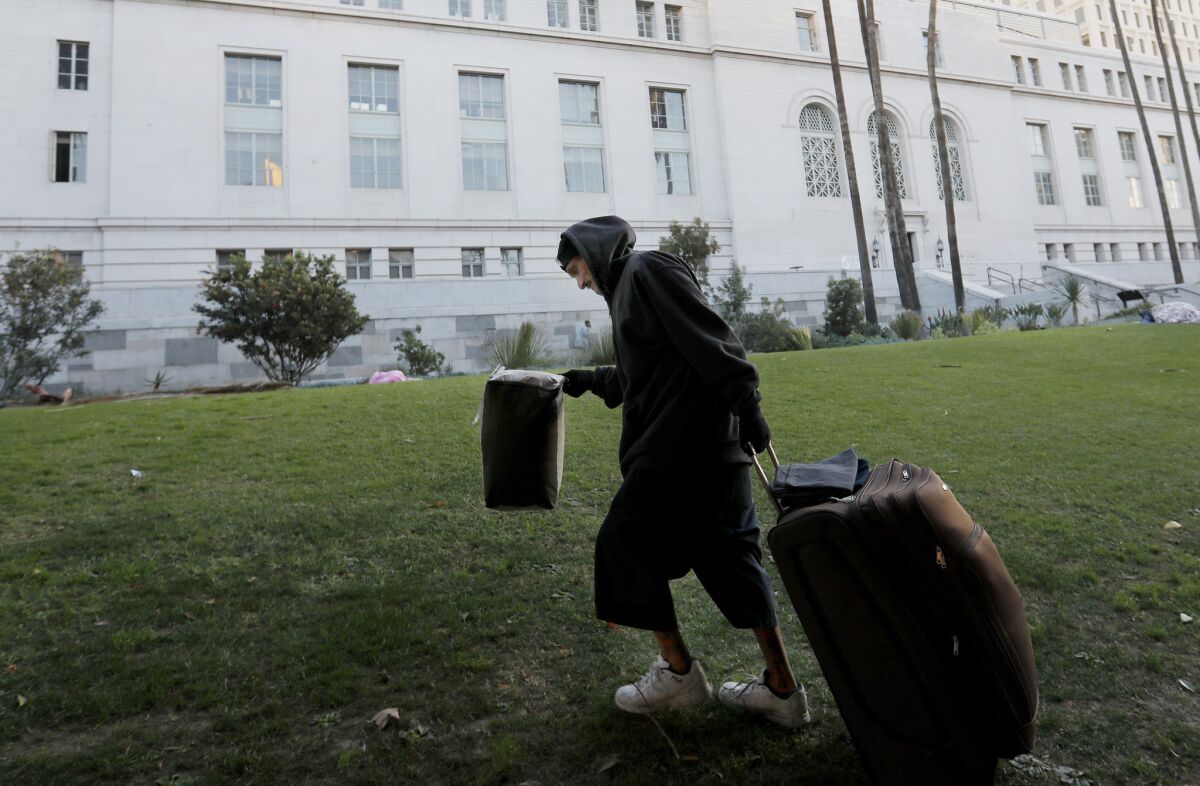 A man pulls his suitcase and other belongings onto the lawn in front of City Hall in Los Angeles.