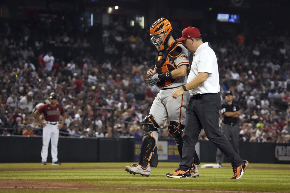 San Francisco Giants catcher Buster Posey leaves the game with a trainer after getting hit with the ball in the sixth inning of a baseball game against the Arizona Diamondbacks, Sunday, July 4, 2021, in Phoenix. (AP Photo/Rick Scuteri)