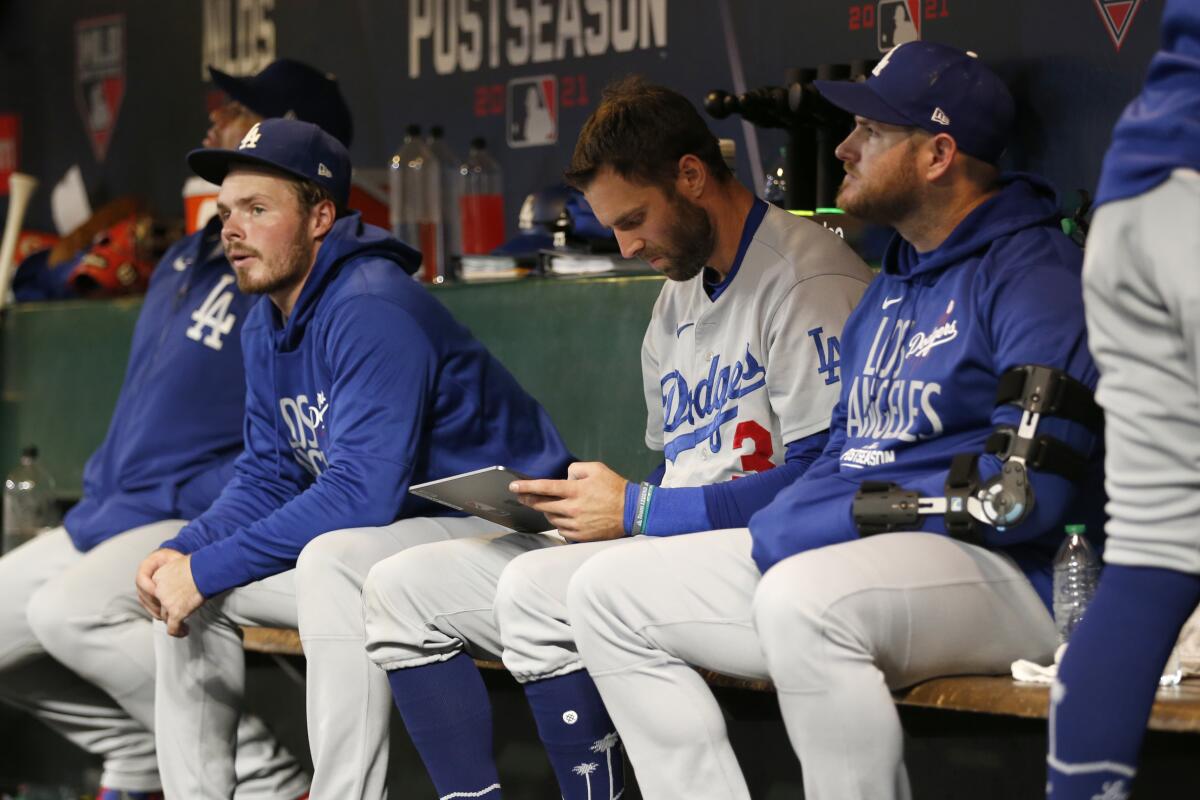 Injured Dodgers first baseman Max Muncy, far right, sits in the dugout with teammates.