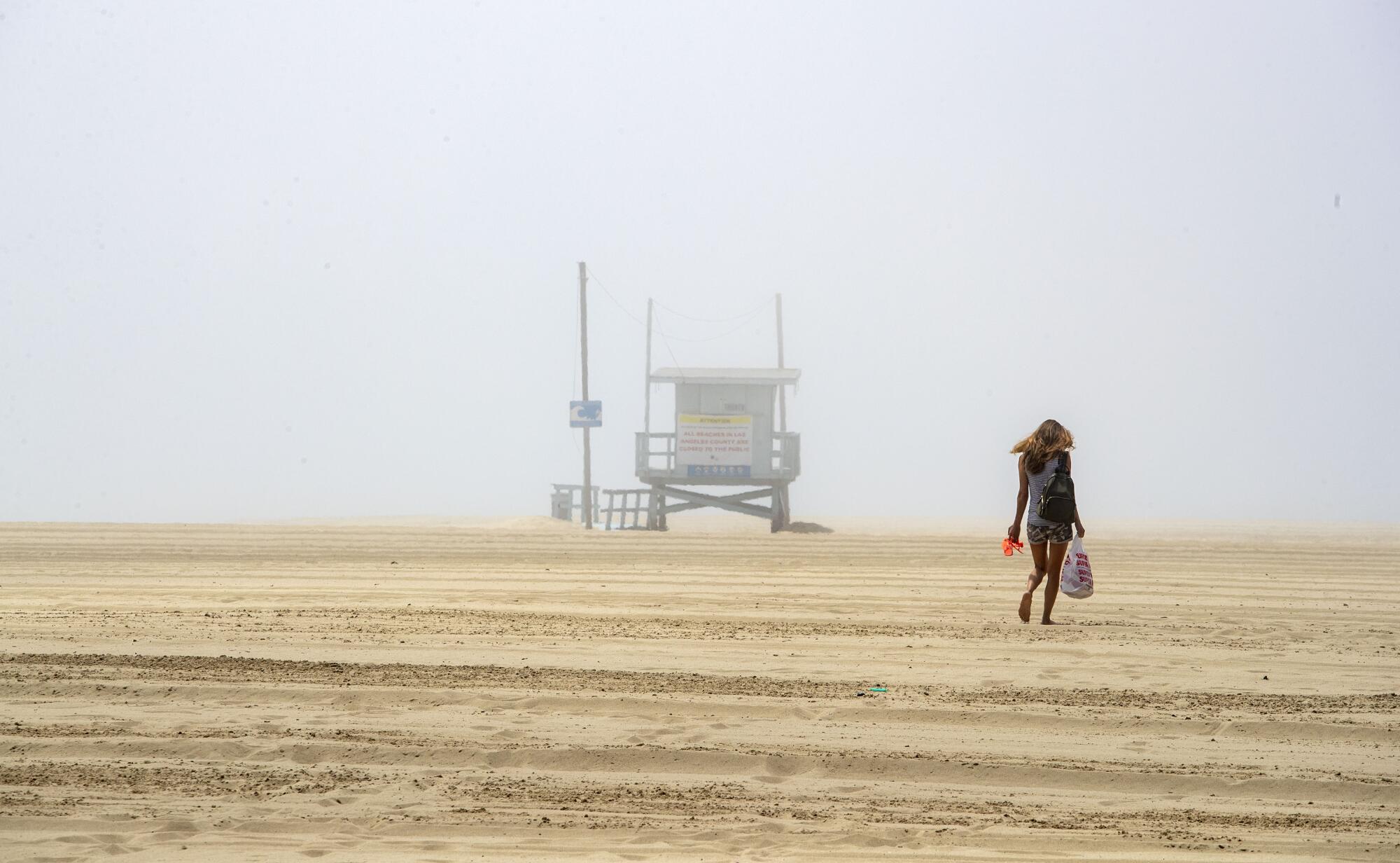A woman walks on the sand in Venice despite law enforcement efforts to keep people off closed Los Angeles County beaches.