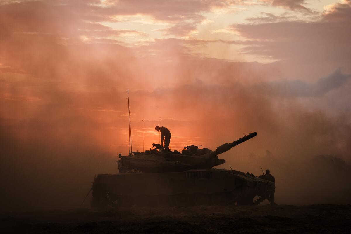 A silhouette of a soldier standing on top of a tank in the desert amid dust and haze.