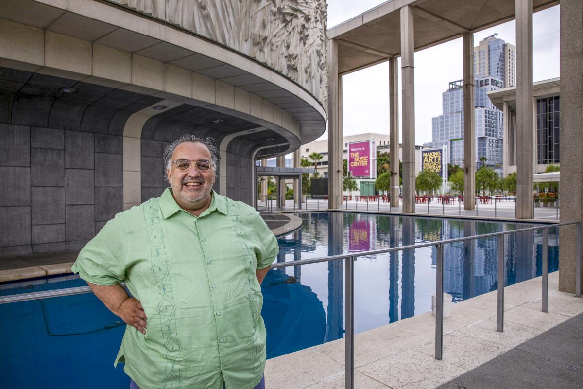 Luis Alfaro stands before the reflecting pool in front of the circular Mark Taper Forum building