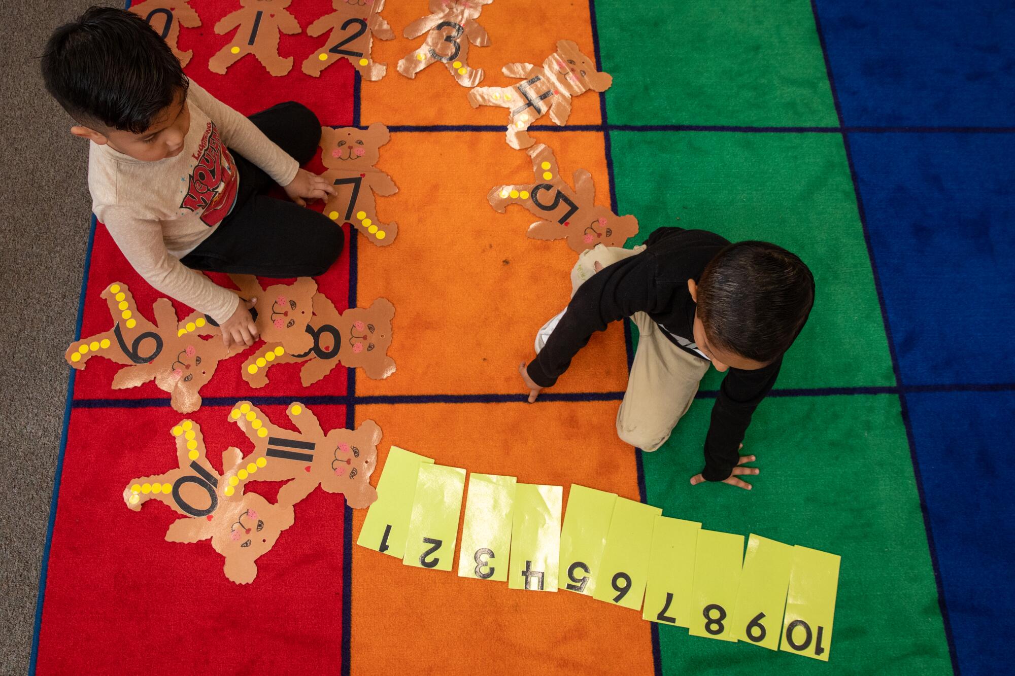 Two small children in a classroom with numbered teddy bear cutouts and corresponding numerals.