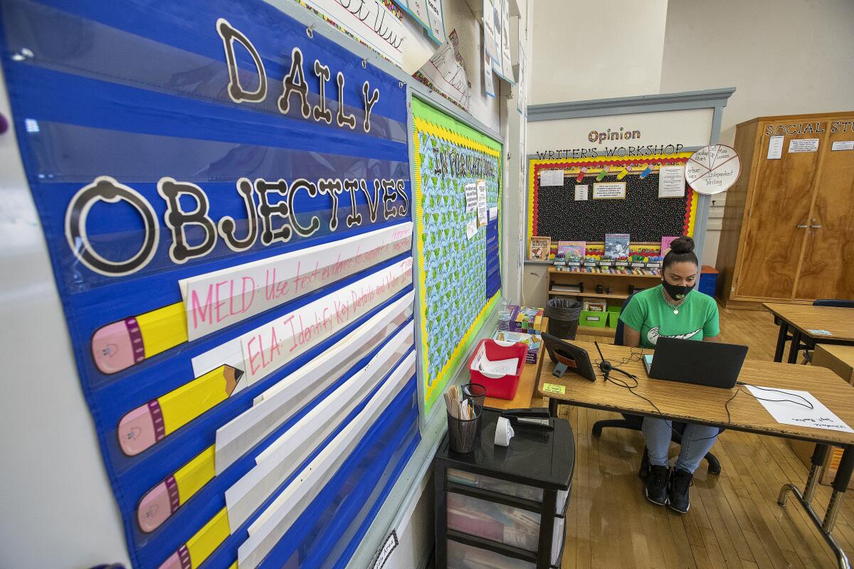 A teacher sits at a classroom in front of a computer