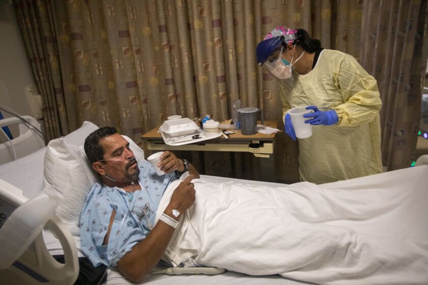 TORRANCE, CA - JULY 30: Kim Dimaunahan Telemetry Oncology RN, right, brings medication to covid positive patient Eustacio Garcia, 54, left, in the covid unit inside Little Company of Mary Medical Center Friday, July 30, 2021 in Torrance, CA. Today the hospital has 20 covid possitive patients. In June they had none. The majority of their covid possitive cases are non vaccinated patients. (Francine Orr / Los Angeles Times)