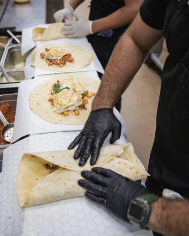 Gloved hands fold a burrito in an assembly line. 