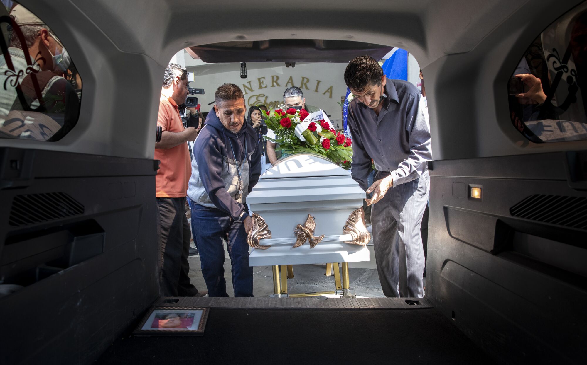 Two men place a casket of a woman in a hearse.