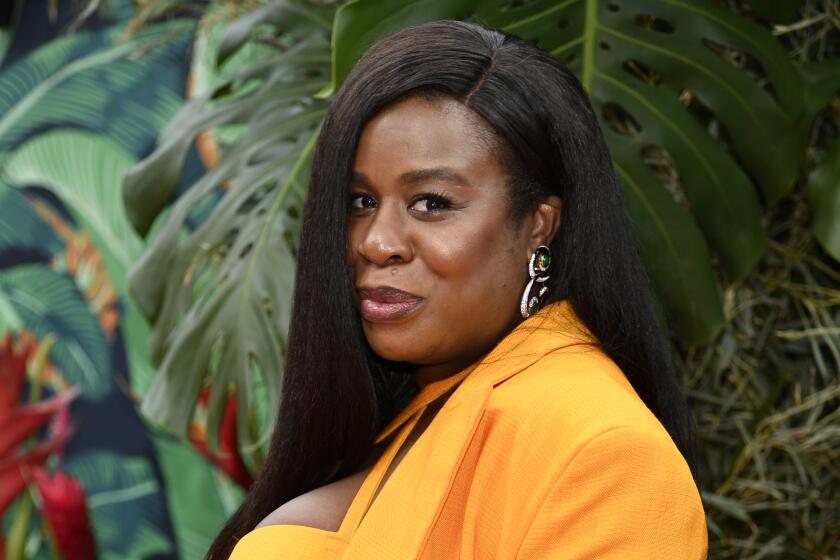 Uzo Aduba holds her growing baby bump while wearing an orange three-piece suit