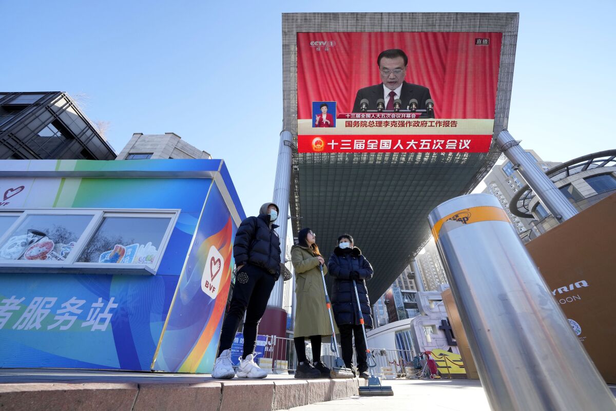 People gather near a large video screen at a shopping mall showing Chinese Premier Li Keqiang speaking during the opening session of the annual meeting of China's National People's Congress (NPC) in Beijing, Saturday, March 5, 2022. (AP Photo/Ng Han Guan)
