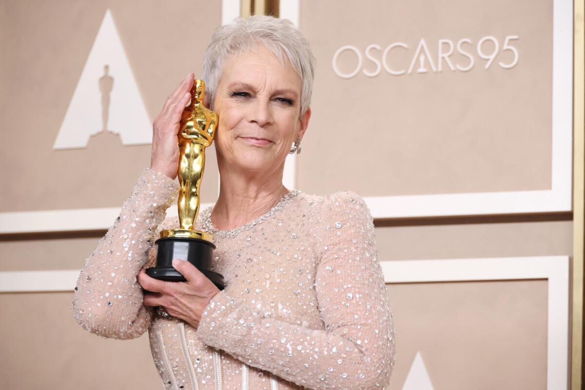 A woman with short gray hair wearing a sparkly dress and holding a gold Oscar trophy against her cheek