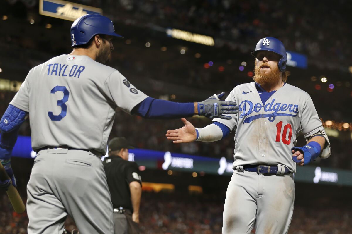 Los Angeles Dodgers' Justin Turner, right, is congratulated by Chris Taylor after scoring against the San Francisco Giants during the ninth inning of Game 5 of a baseball National League Division Series Thursday, Oct. 14, 2021, in San Francisco. (AP Photo/Jed Jacobsohn)