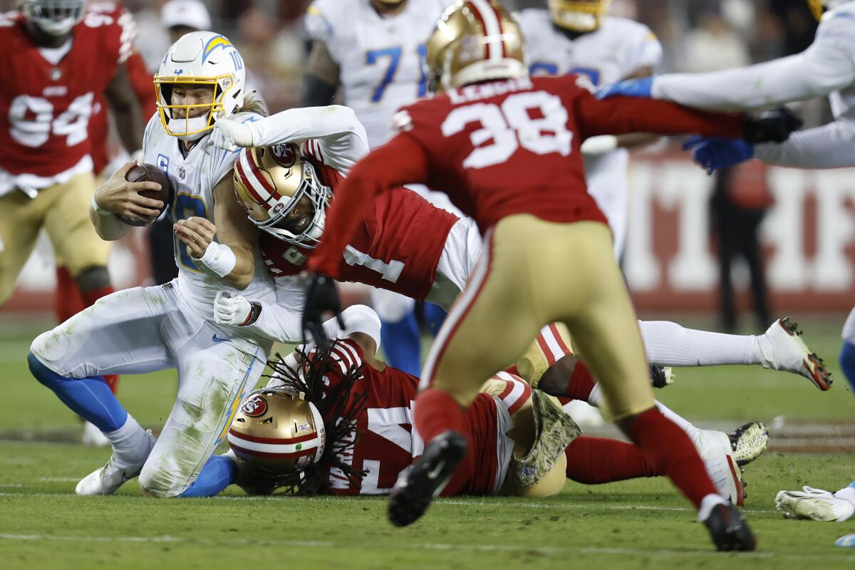 Chargers quarterback Justin Herbert (10) is hit by 49ers Jimmie Ward (1) and Fred Warner (54) in the first half.