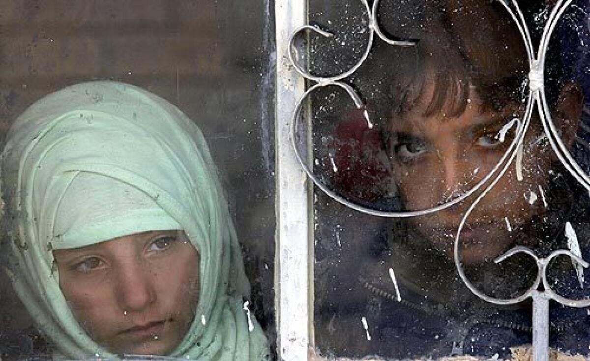 Iraqi children watch through a window as U.S. soldiers search their home.