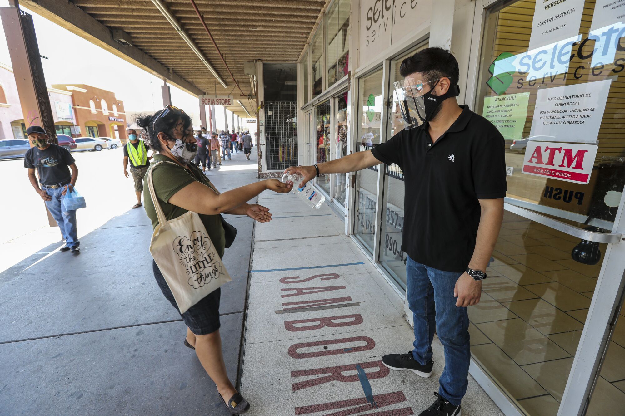 Emmanuel Vazquez squirts hand sanitizer into a woman's hand outside a private service agency in Calexico.