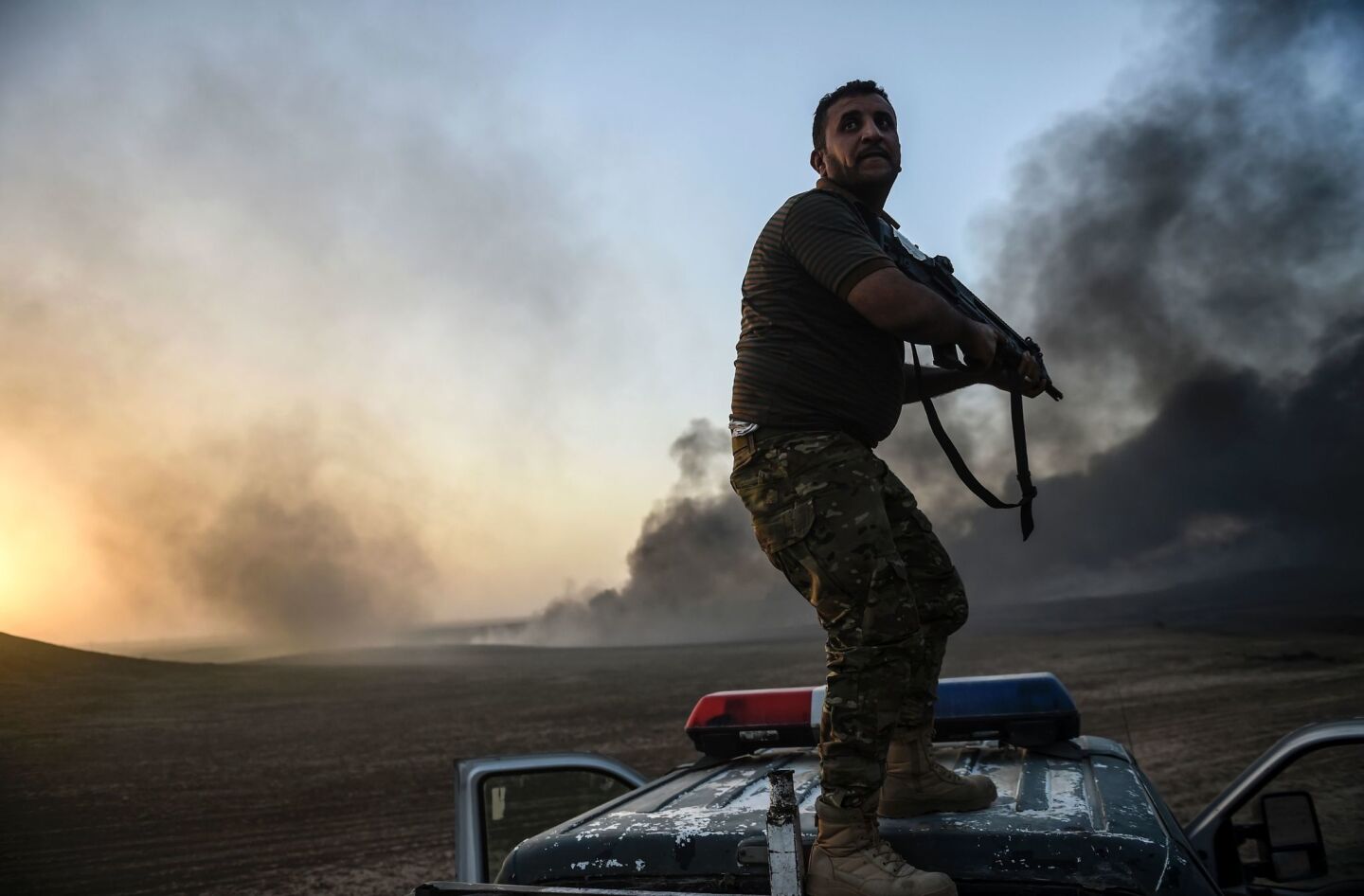 An Iraqi fighter takes a position on top of a vehicle as smoke rises on the outskirts of the Qayyarah area, 35 miles south of Mosul, during an operation against Islamic State.