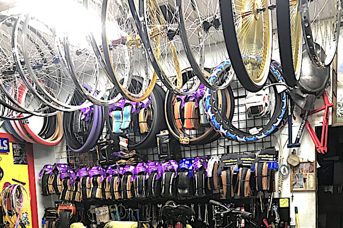 A row of bikes hanging from the ceiling of a shop over a wall filled with gear