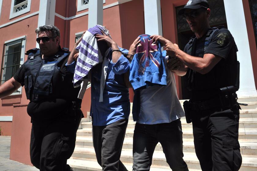 Greek police officers flank two Turkish military officers who appeared before a prosecutor in Alexandroupoli. They were among eight members of the Turkish military who flew to Greece in a helicopter and requested asylum.