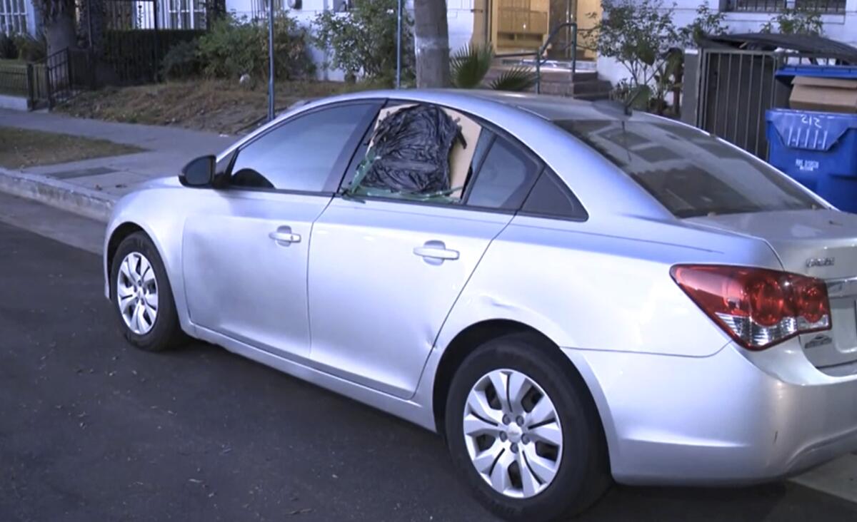 A silver car has cardboard and plastic over a broken window.