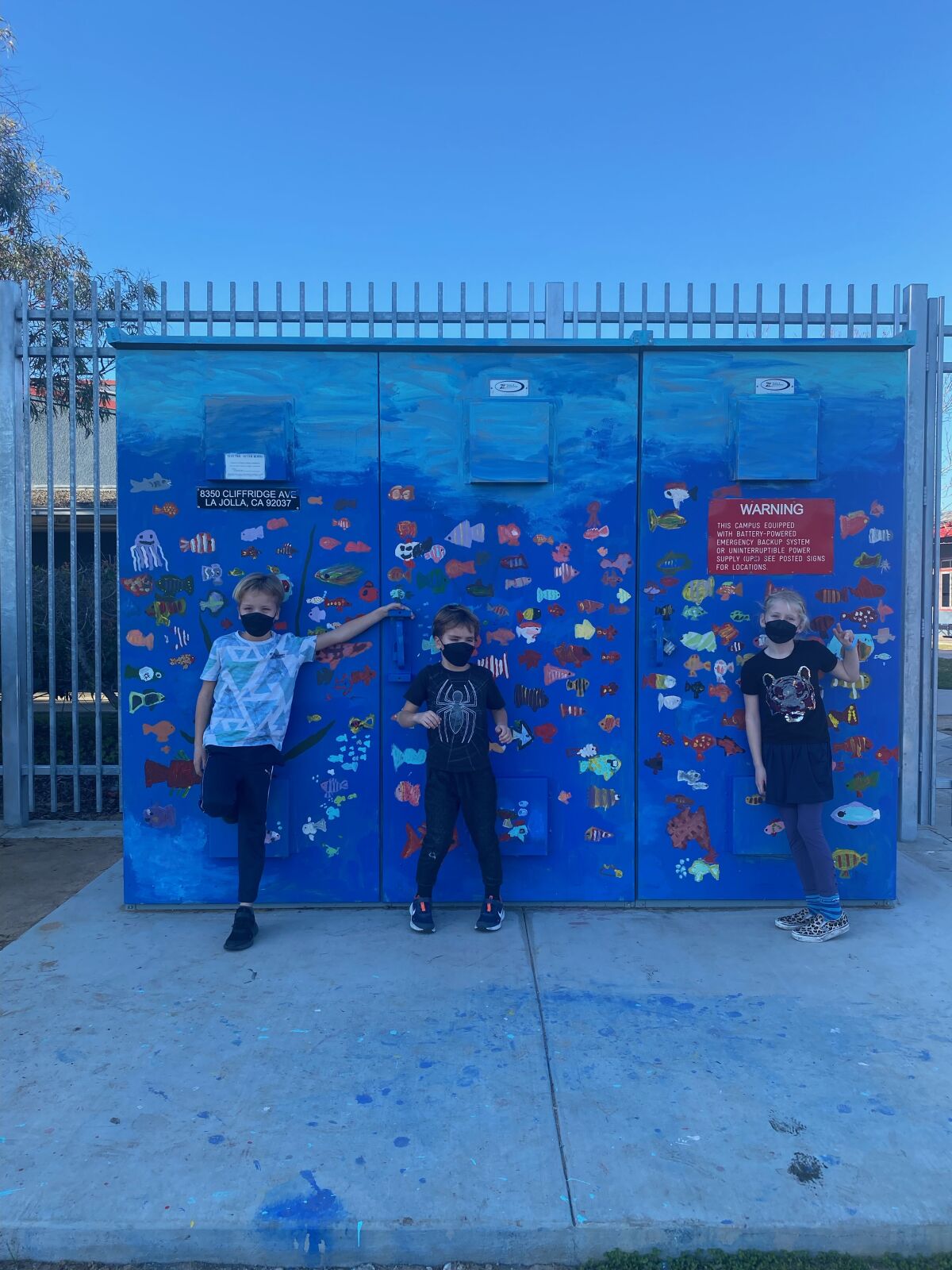 Eric and Ben Sorensen and Rebecca Weibel show electrical boxes they helped paint outside Torrey Pines Elementary School.