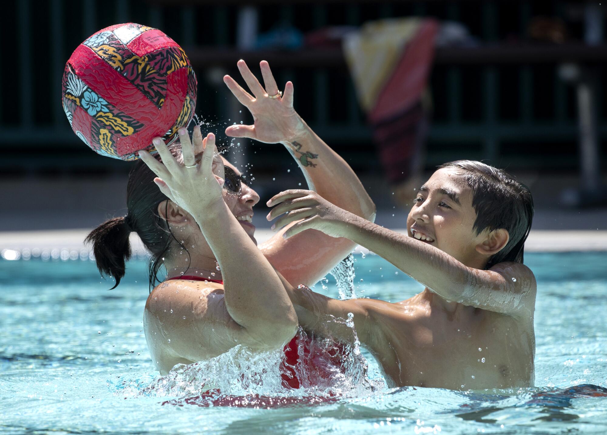A woman and boy play with a ball in a swimming pool