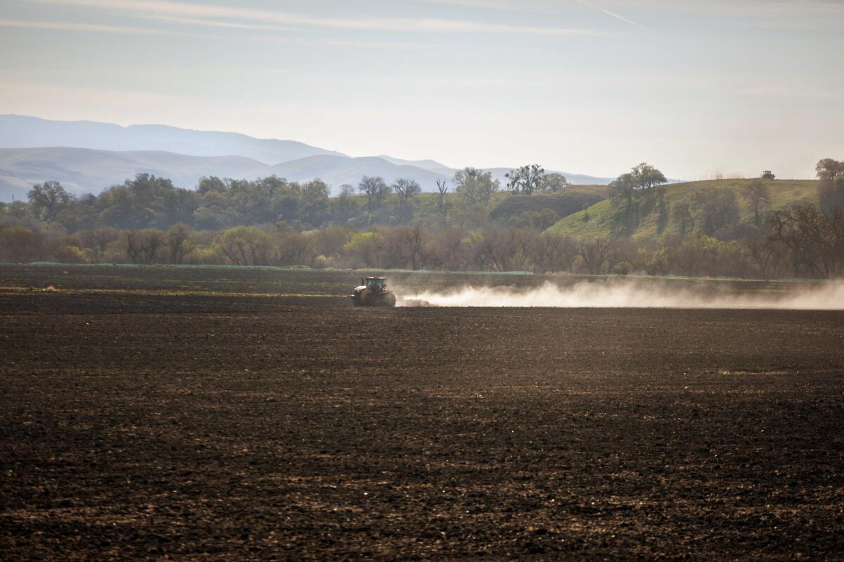 A tractor plows a field, leaving a plume of dust in its wake